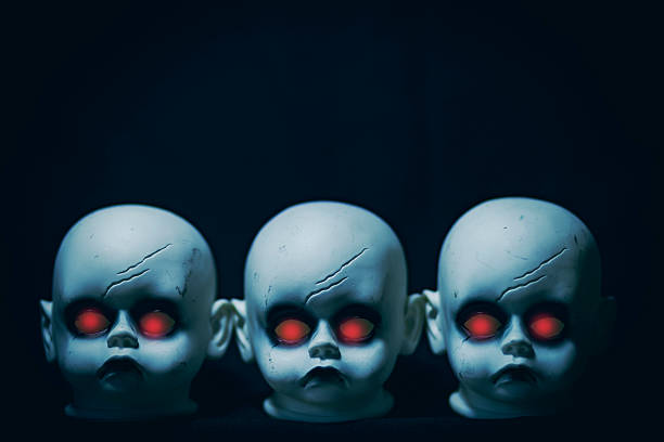 A row of three creepy doll heads with red glowing eyes.