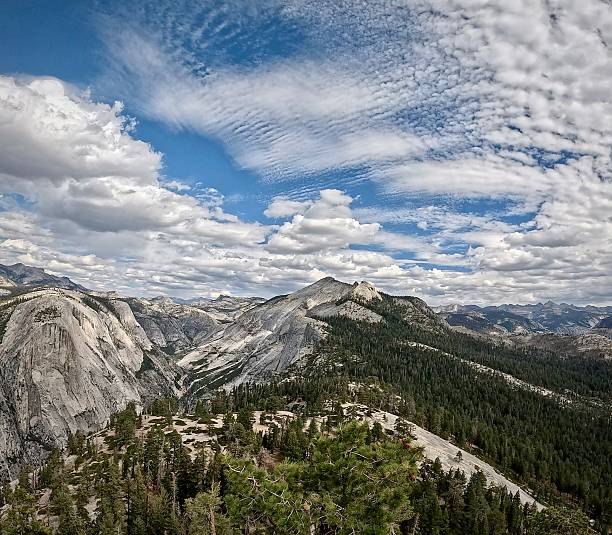 A panoramic view opens up toward layered granite domes and valleys beneath a sculpted sky on the way to Half Dome.