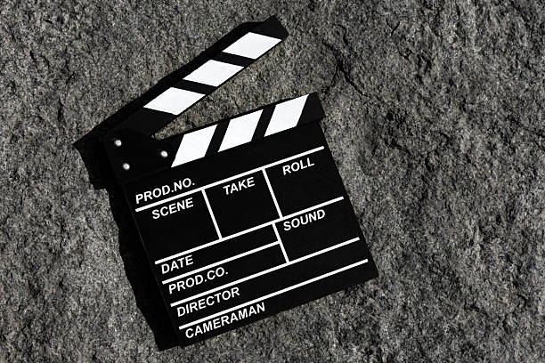A classic film clapperboard lies flat on a textured grey stone background. Shot from above, the image blends industrial minimalism with cinematic symbolism