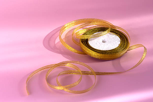 A delicate, sparkling gold ribbon lies gracefully on a light pink background, creating elegant curves and soft shadows.