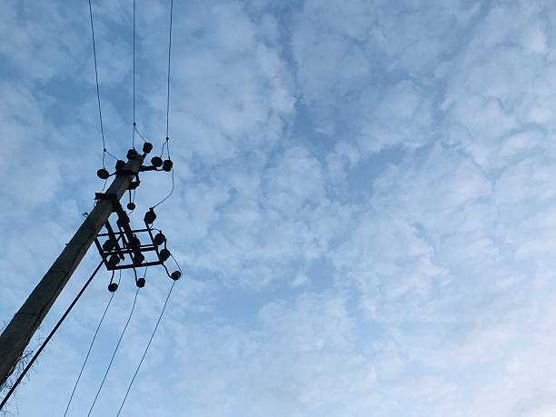 Power lines rise against a backdrop of a textured blue sky filled with soft, white clouds in a peaceful rural area during daytime.