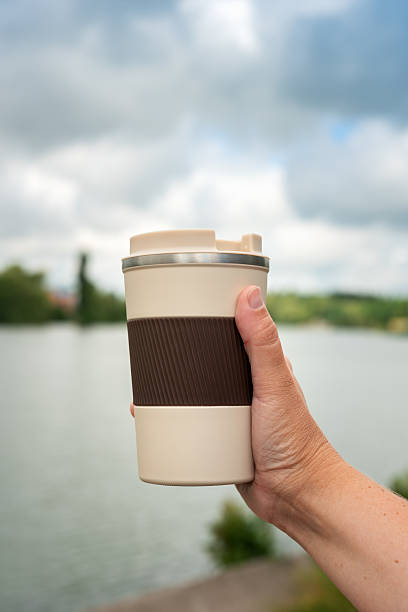 istock Hand holding a reusable thermo coffee cup near a peaceful river, surrounded by nature 2226664719