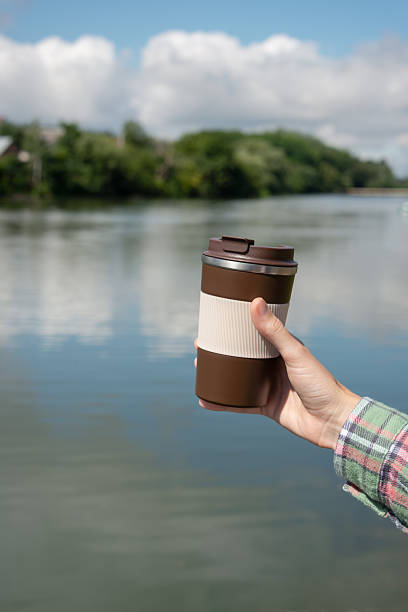 istock Hand holding a reusable thermo coffee cup near a peaceful river, surrounded by nature 2226664953