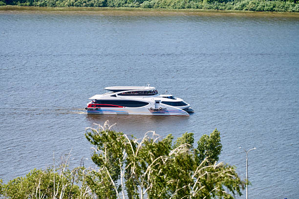 Nizhny Novgorod, Russia - June 9, 2025 - Sleek modern boat glides on Volga river. Bright sunlight highlights calm waters, with lush green foliage framing scene