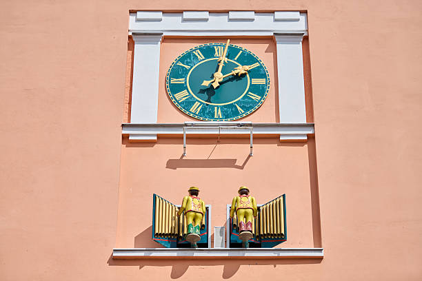 Gvardeysk, Russia - May 13, 2025 - Town hall facade features prominent clock. Below, mechanical dolls in vibrant clothing emerge, adding musical charm to structure. Peach walls enhance visual appeal