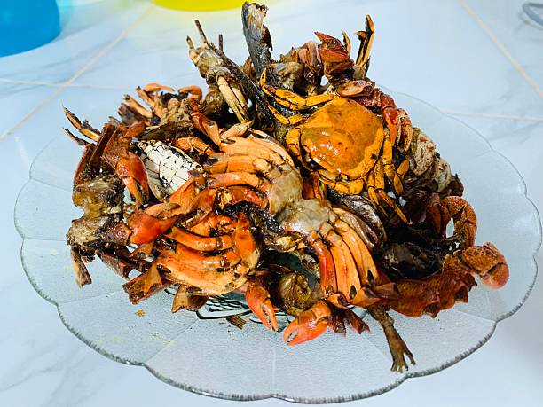 A glass plate filled with freshly cooked crabs showcasing vibrant orange shells and a delicious seafood meal prepared for consumption on a smooth surface.