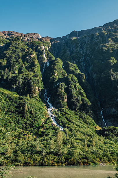 istock Multiple waterfalls cascading down a steep lush green cliff mountainside with clear blue sky in Hyder Alaska near Fish Creek, USA 2226671110