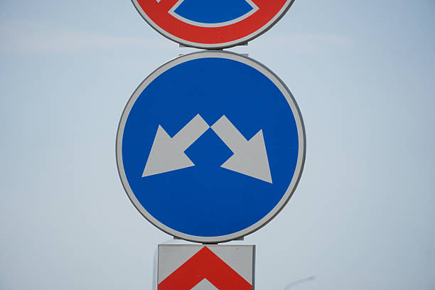 istock Two white arrows on a blue circular sign indicate that vehicles must choose separate paths. The sign is positioned prominently against a bright sky 2226673577