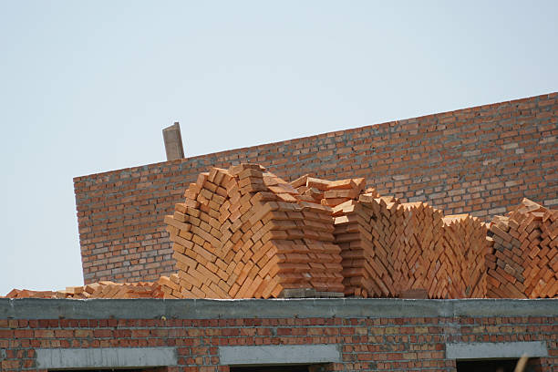 Stacked bricks rest atop a partially constructed building at a construction site, with bright sunlight illuminating the scene during the day.