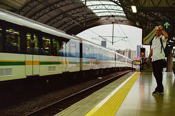 A man stands at a train station platform with his hand on his head as a commuter train passes, showcasing urban transportation and dynamic travel moments in a bustling city setting. Taken in Medellín, Colombia on 35mm Film.
