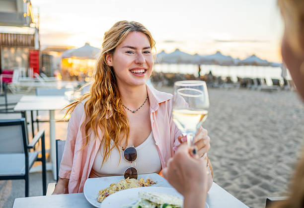 istock Two young women toasting with white wine at beach restaurant 2226683345