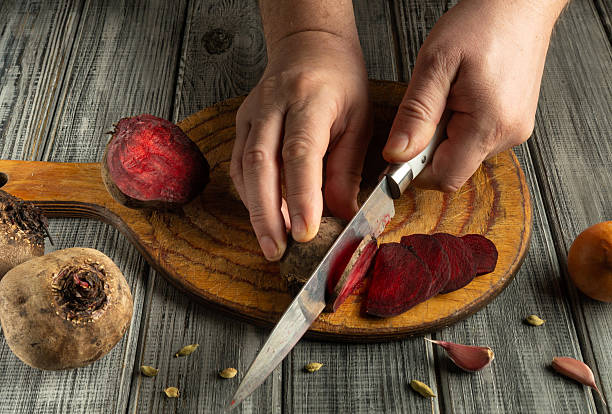 istock Hands skillfully slice vibrant beets and garlic on a wooden cutting board, with other vegetables nearby, showcasing the art of food preparation in a warm kitchen atmosphere 2226683781