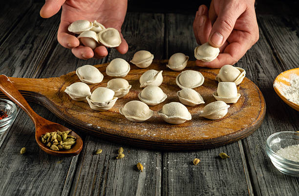 istock Hands skillfully shape and arrange dumplings on a wooden board. Various spices and flour are placed on a rustic kitchen table, showcasing traditional cooking techniques 2226683884