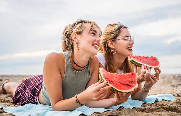 istock Two smiling young women lying on beach towel, eating watermelon 2226684461