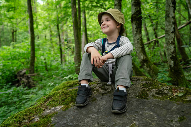 istock Smiling Young Boy Sitting on a Mossy Rock in a Lush Forest 2226696792