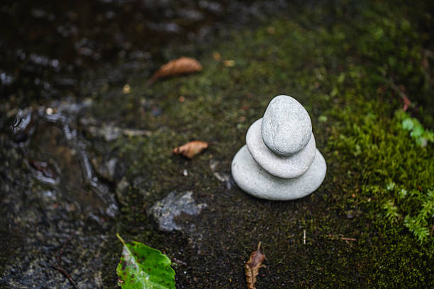 Three grey stones stacked in balance atop a lush green mossy surface, symbolizing tranquility, natural harmony, and mindfulness against a tranquil forest setting.