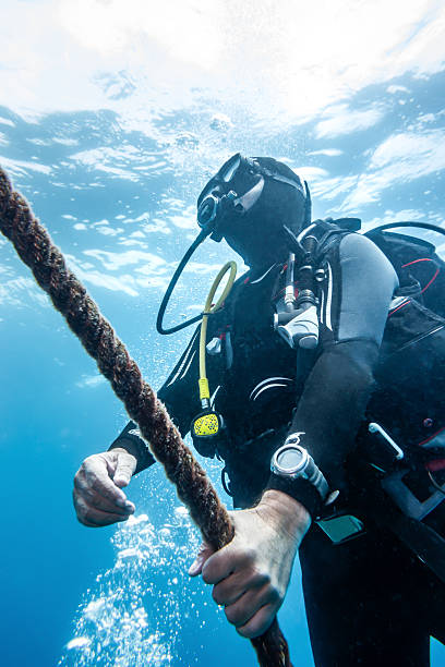Scuba diver ascending in the Mediterranean Sea, grasping a rope while gazing up towards the surface, surrounded by rising air bubbles in a vibrant underwater world