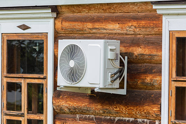 istock Modern air conditioner unit installed on the exterior wall of a rustic log house between vintage wooden windows, blending technology with tradition. 2226703265