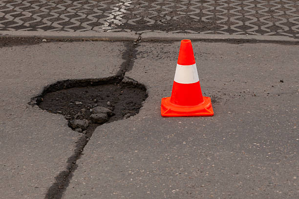 istock Road hazard: traffic cone marking deep pothole. Damaged asphalt with safety cone as warning sign. Road maintenance issue 2226704146