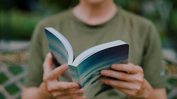 istock Young  man reading a book while relaxing in the morning in a public park. 2226726374