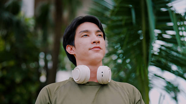 istock Young Asian man putting on headphone while enjoying peaceful moment in public park. 2226726382