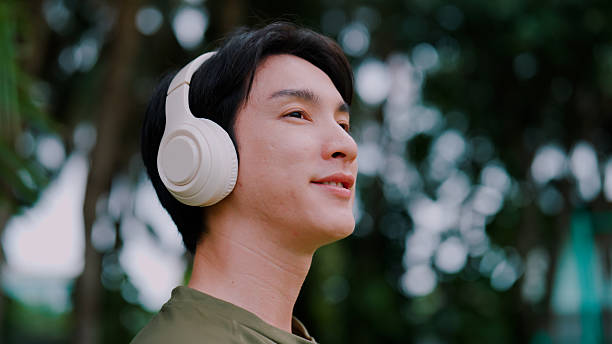 istock Young Asian man putting on headphone while enjoying peaceful moment in public park. 2226726388