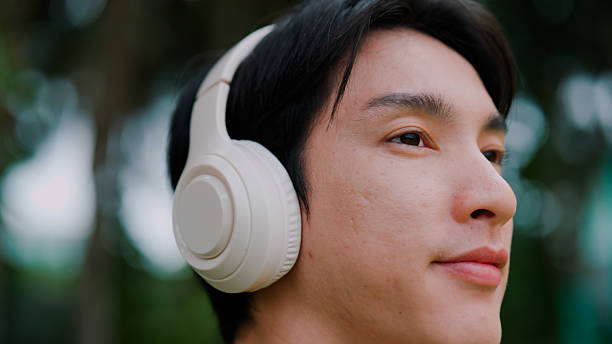 istock Young Asian man putting on headphone while enjoying peaceful moment in public park. 2226726389