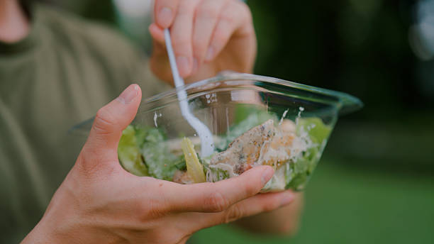Young man eating salad while sitting on a bench in a public park.