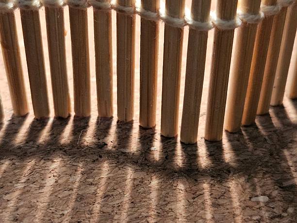 istock Close-up of a black shadow created by a bamboo sushi rolling mat that is standing upright on a cork backdrop. 2226727624