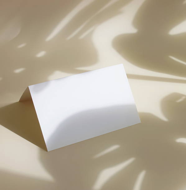 istock Folded paper blank sheet card mockup with copy space and monstera leaves shadow on beige background . 2226731564