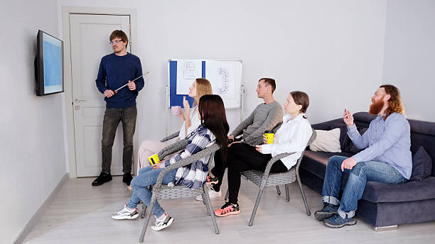 A successful company manager makes a presentation in front of his colleagues. A group of people is sitting in a conference room of a family office and watching a TV screen.
