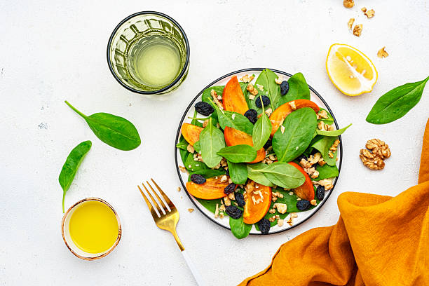 istock Autumn vegan persimmon salad with walnuts, blue raisin and spinach, white background, top view 2226739706