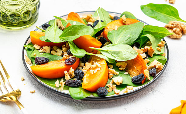 istock Autumn vegan salad with fresh persimmon, walnuts, raisin and spinach, white background, top view 2226739710