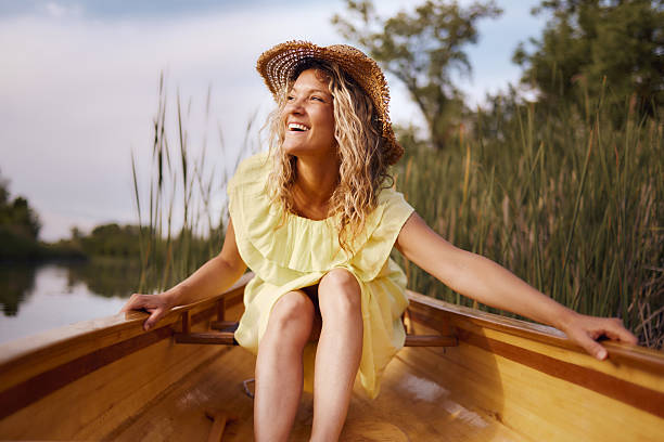 Young happy woman in a dress enjoying while spending a summer day in a canoe at lake.