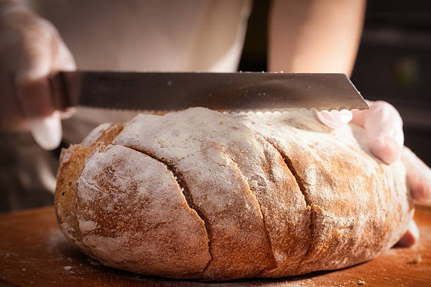 istock Baker Slicing a Freshly Baked Loaf of Bread with a Sharp Knife 2226743460