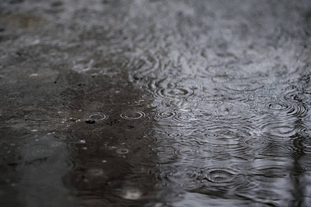 istock raining on the concrete walk way full with rain droplets splash ring bounce off the surface of water with reflected of white cloudy sky 2226745164