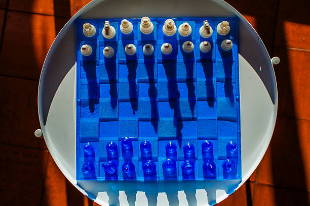 A transparent blue chessboard with contrasting white and blue pieces casts sharp shadows, creating a visually striking  arrangement