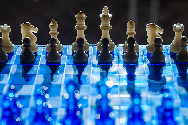 A dramatic chessboard scene with contrasting black and white pieces on a reflective blue surface, emphasizing strategy and focus