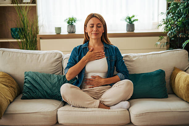 istock Serene woman practicing deep breathing exercise on sofa at home 2226750646