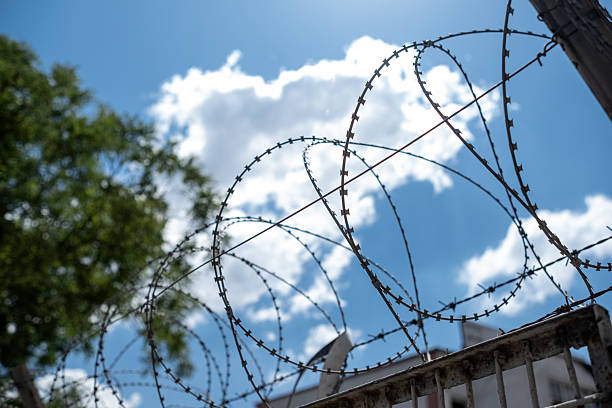 istock Barbed Wire Stretches Against a Bright Blue Sky With Clouds in a Secure Location Indicating Barriers and Confinement 2226750751