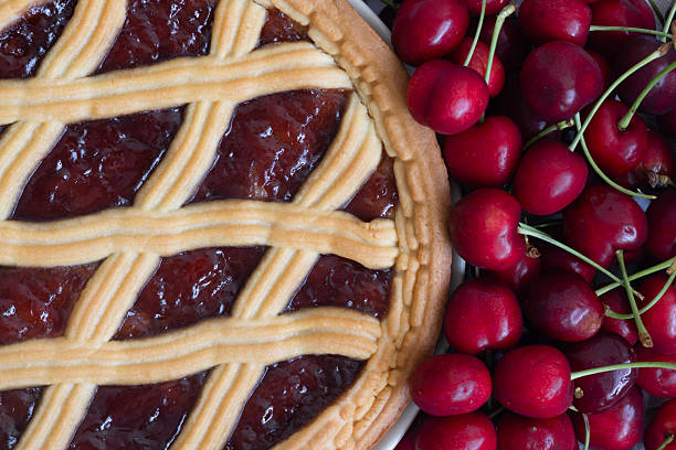A cherry pie features a lattice crust next to fresh, ripe cherries.