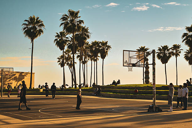 People playing basketball at the iconic Venice Beach outdoor courts as the sun sets behind the palm trees, Los Angeles, California, USA