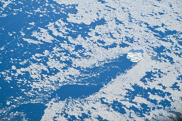 Aerial close-up view of broken sea ice floating in the Arctic Ocean near the coast of Greenland, with a single large iceberg visible among the frozen fragments