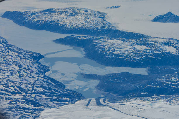 Aerial view of a deeply frozen fjord in central Greenland, surrounded by snow-covered cliffs and ice flows, illustrating the harsh Arctic environment