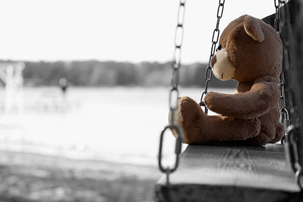 Lonely teddy bear on swing near river, space for text