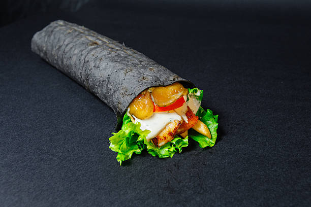 A black tortilla wrap with lettuce and chicken on black surface
