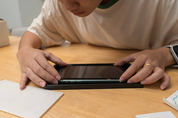 istock Person closely inspecting smartphone while installing tempered glass screen protector on wooden surface 2226758149