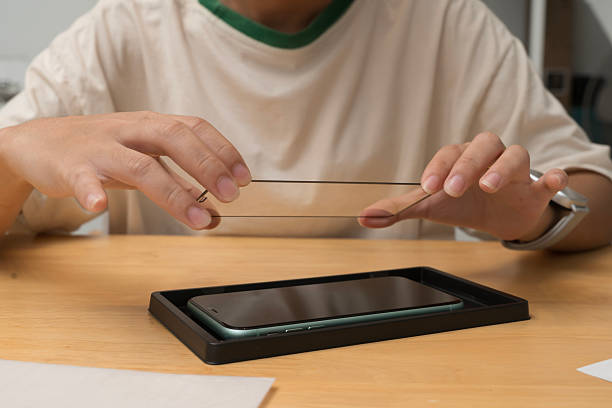 istock Hands placing tempered glass screen protector onto smartphone during installation process on wooden surface 2226758154