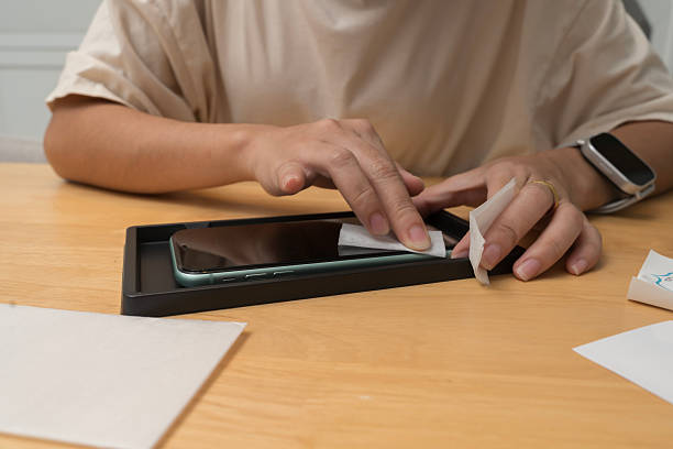 istock Hand cleaning smartphone screen with wet wipe before installing screen protector on wooden table surface 2226758402
