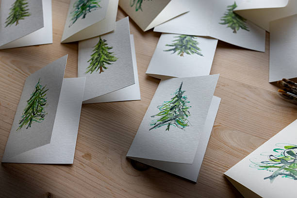 A close-up shot of a collection of handmade Christmas greeting cards featuring watercolour-painted Christmas trees spread across a wooden table. Perfect for holiday crafts, DIY stationery, and festive art themes.Videos are available similar to this scenario.